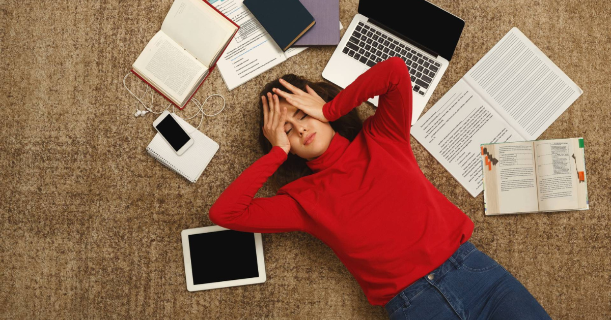 A student laying on the floor, surrounded by books and study notes.